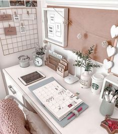 a white desk topped with a laptop computer next to a calendar and potted plants