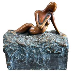 a bronze statue of a woman laying on top of a rock with water flowing over it