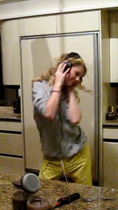 a woman standing in front of a kitchen counter talking on a cell phone