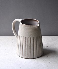 a white ceramic mug sitting on top of a table next to a gray wall and floor