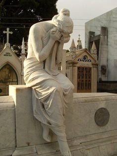 a statue of a man sitting on top of a stone wall next to a cemetery