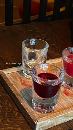 three glasses of liquid sit on a wooden tray