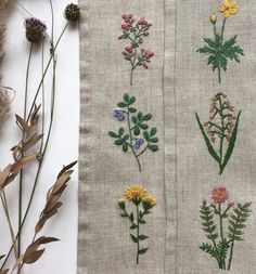 three different types of embroidered flowers on linen and some dried plants in the foreground