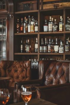 a leather couch sitting in front of a wooden shelf filled with bottles