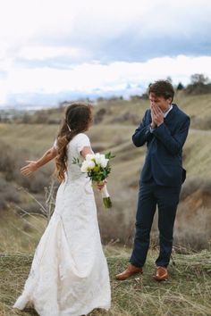 a bride and groom standing in the middle of a field with their hands on their face