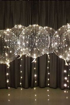 three clear balloons with lights hanging from them on a black curtained room floor in front of curtains