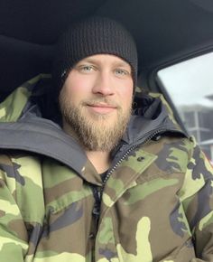 a man with a beard wearing a jacket and beanie sitting in the back seat of a car