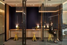 a woman sitting on a chair in front of a glass wall with candles and stools