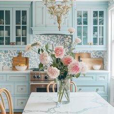 a vase filled with pink flowers sitting on top of a kitchen counter next to a chandelier