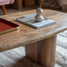 a wooden table with a book and vase on it, sitting in front of a pink chair