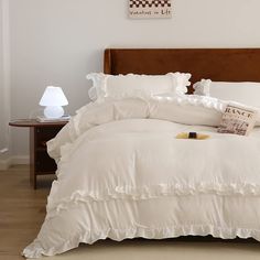 a bed with white sheets and ruffles in a room next to a lamp