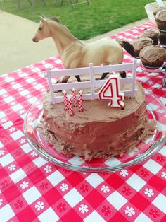 a birthday cake on a table with a horse figurine and cupcakes