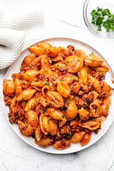 a white plate filled with pasta and meat sauce on top of a marble countertop