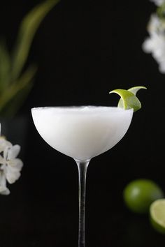 a martini glass with a lime garnish on the rim and white flowers in the background