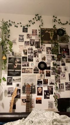 a bedroom wall covered in photos and plants with a guitar on the bed next to it