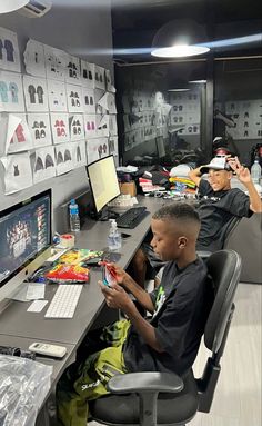 two young boys sitting at a desk in front of a computer monitor and desktop screen