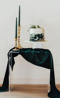 a table with a cake on it and two candles next to it in front of a white wall