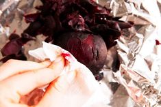 someone is peeling the end of a beet on tin foil with their hand and knife