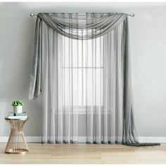 a window with sheer curtains and a small table in front of it on a wooden floor