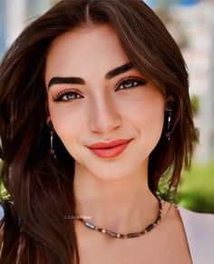 a woman with long brown hair wearing a necklace and earrings, smiling at the camera