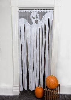 two pumpkins sitting on the floor next to a white curtain with ghost decorations hanging from it