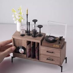 a hand is holding a record player in front of a wooden cabinet