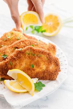 someone is sprinkling parmesan cheese on top of some fried fish with lemon wedges