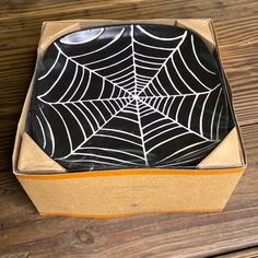 a black and white spider web plate in a cardboard box on a wooden table top