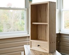 a wooden cabinet sitting on top of a table in front of a window with two windows