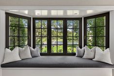 a window seat with pillows on it in front of a large window that looks out onto a lake