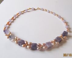 Pearl and Amethyst necklace woven into a floral pattern. Large cube of Amethyst has been woven with graduated sized rice Cultured Freshwater pearls in a lovely Apricot/Peach colour. The largest ones are at the front and measure 6x9mm to 7/8x5mm. The overall effect is a vintage style necklace with high visual impact.The cubes of Amethyst are substantial and measure 10mm. The other Amethyst are rounds and measure 8mm. They are matched with rice pearls measuring graduated from 9x6mm to 8x5mm. All t Elegant Handmade Amethyst Pearl Necklace, Purple Single Strand Pearl Jewelry, Purple Pearl Single Strand Necklace, Purple Pearl Single Strand Jewelry, Elegant Lavender Necklaces With Gemstone Beads, Handmade Elegant Amethyst Beaded Necklaces, Handmade Elegant Purple Pearl Necklace, Elegant Lavender Beaded Necklace With Natural Stones, Purple Pearl Jewelry With Natural Stones