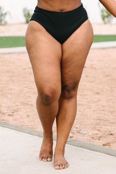 a woman in a black swimsuit walking down the sidewalk with her hand on her hip