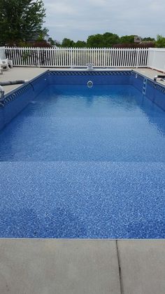 an empty blue swimming pool with white fence and lawn chairs in the backround