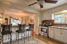 a kitchen with white cabinets and black bar stools next to a stove top oven