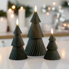 three small christmas trees sitting on top of a white table next to candles in front of them