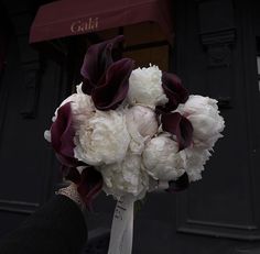 a bridal bouquet with white and purple flowers in front of a storefront window