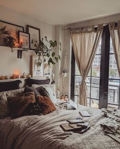 an unmade bed with lots of pillows and blankets in front of a large window