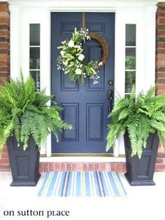 two large planters are on the front porch next to a blue door with white trim