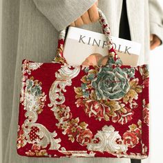 a woman holding a red purse with a name tag in it's center and an ornamental pattern on the front