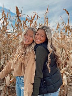 two girls standing in front of a corn field smiling at the camera with their arms around each other