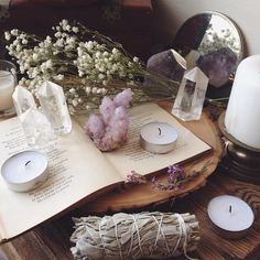 an open book sitting on top of a wooden table next to candles and flowers in vases