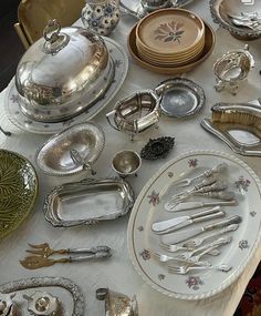 a table topped with lots of silverware on top of a white cloth covered table