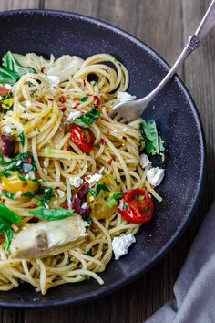 a black bowl filled with pasta and veggies on top of a wooden table