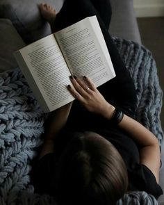 a woman is reading a book while laying on a couch with her legs crossed out