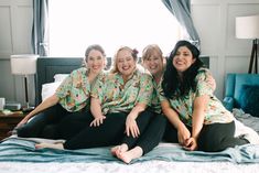 three women sitting on top of a bed smiling for the camera while wearing matching shirts