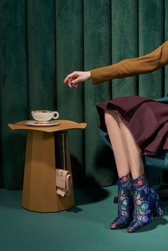 a woman is sitting on a chair with her legs crossed and holding a coffee cup