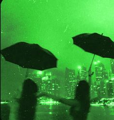 two people holding umbrellas in front of a cityscape at night with green light