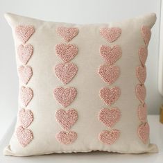 a pink and white pillow with hearts embroidered on the front, sitting on a table