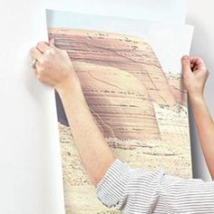 a man is holding up a photograph on the wall with his hands and arm in front of him