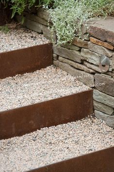 stone steps lead up to a planter filled with rocks and gravel in front of a rock wall